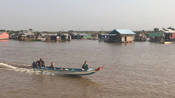 Un barco de pesca, con la red sumergida, navega por el Tonlé Sap, un sistema de lago y río de agua dulce, con un pueblo flotante a la distancia.